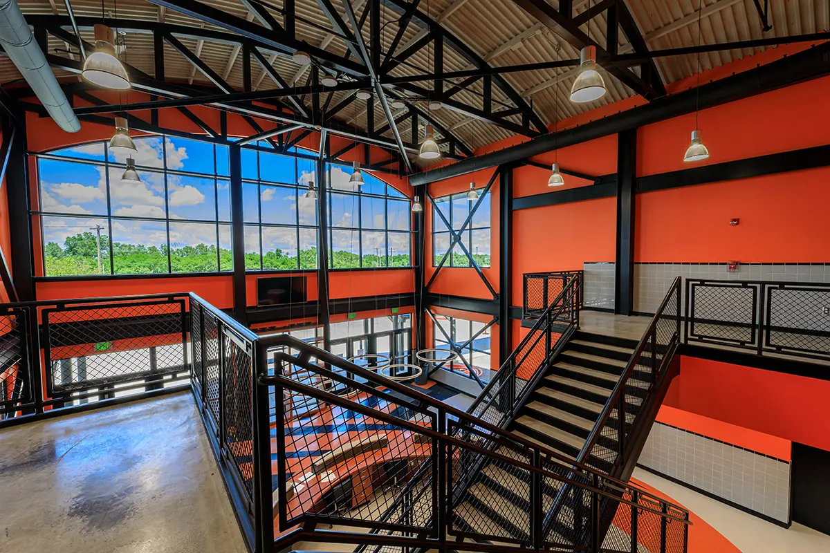 Spacious modern interior with orange and black accents. Large windows offer a view of greenery, and metal staircases create an industrial feel.