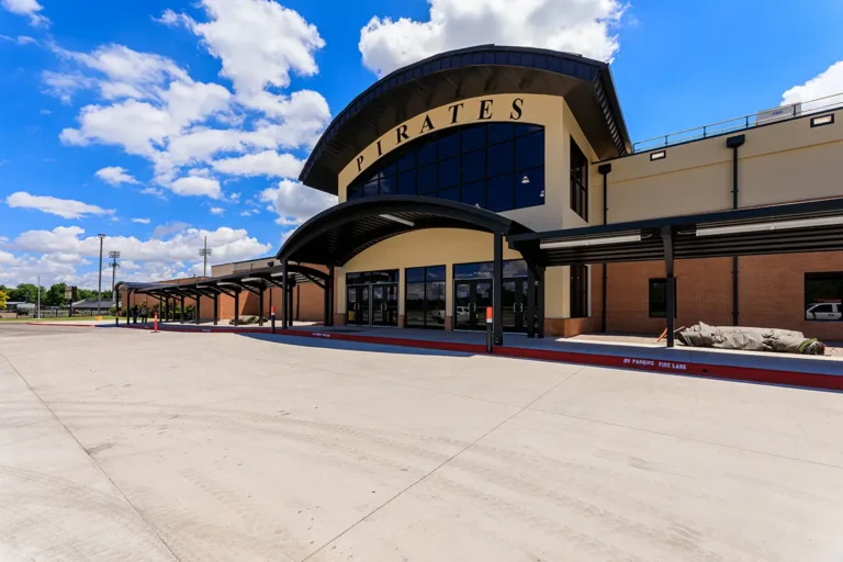 Modern school entrance with "PIRATES" sign, featuring a sleek, arched canopy. A bright, clear sky with fluffy clouds adds a welcoming, energetic tone.