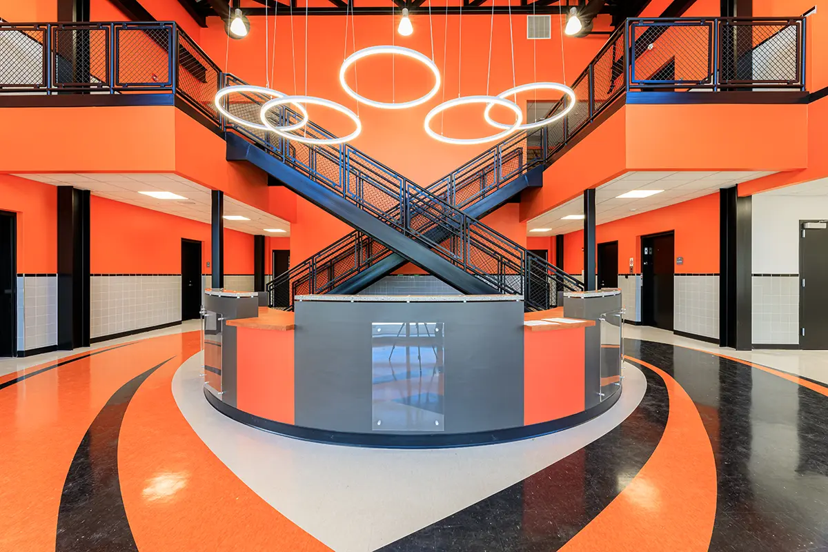 Modern lobby with striking orange and black design, featuring a central staircase and circular ceiling lights. Sleek, contemporary, and vibrant atmosphere.