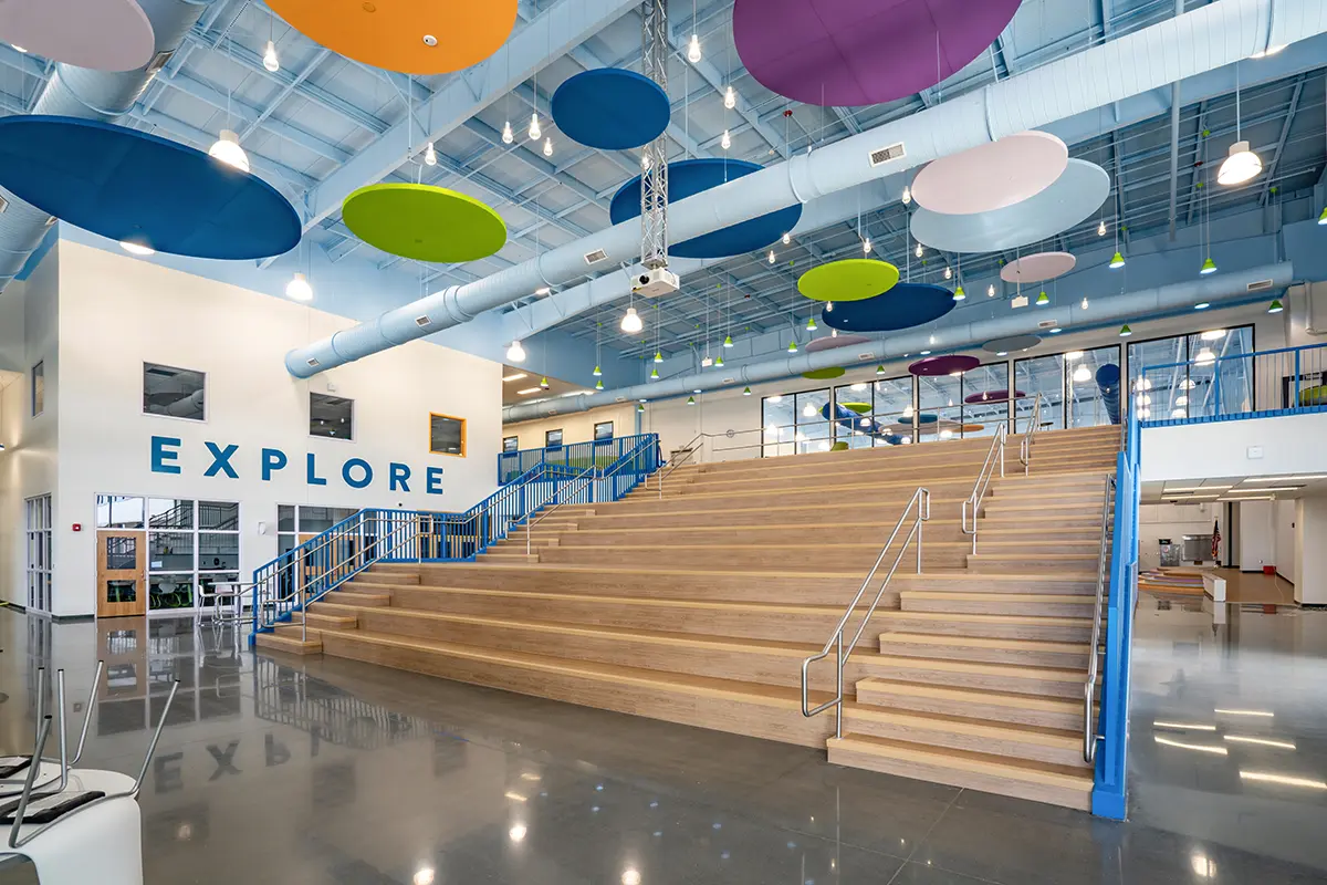 Modern interior with wide wooden staircase, colorful circular ceiling panels, and large "EXPLORE" text on the wall. Bright, inviting atmosphere.