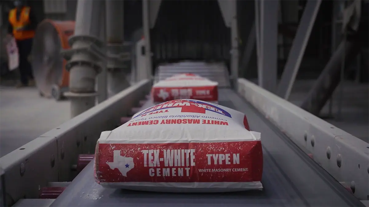 Aerial view of an industrial facility with three large white domes connected by metal structures. Surrounding area includes vehicles and machinery by the water.