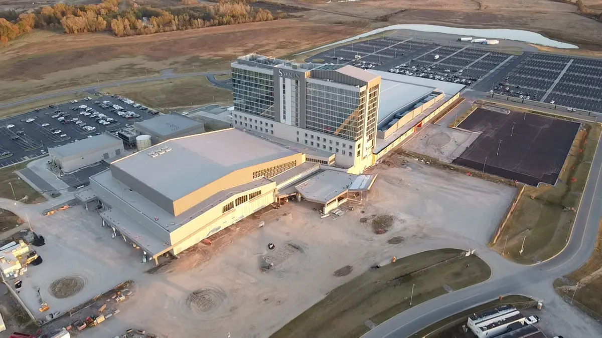 Aerial view of a large, modern building complex with a hotel tower labeled "S... X" in a rural landscape. Surrounding parking lots are mostly empty.