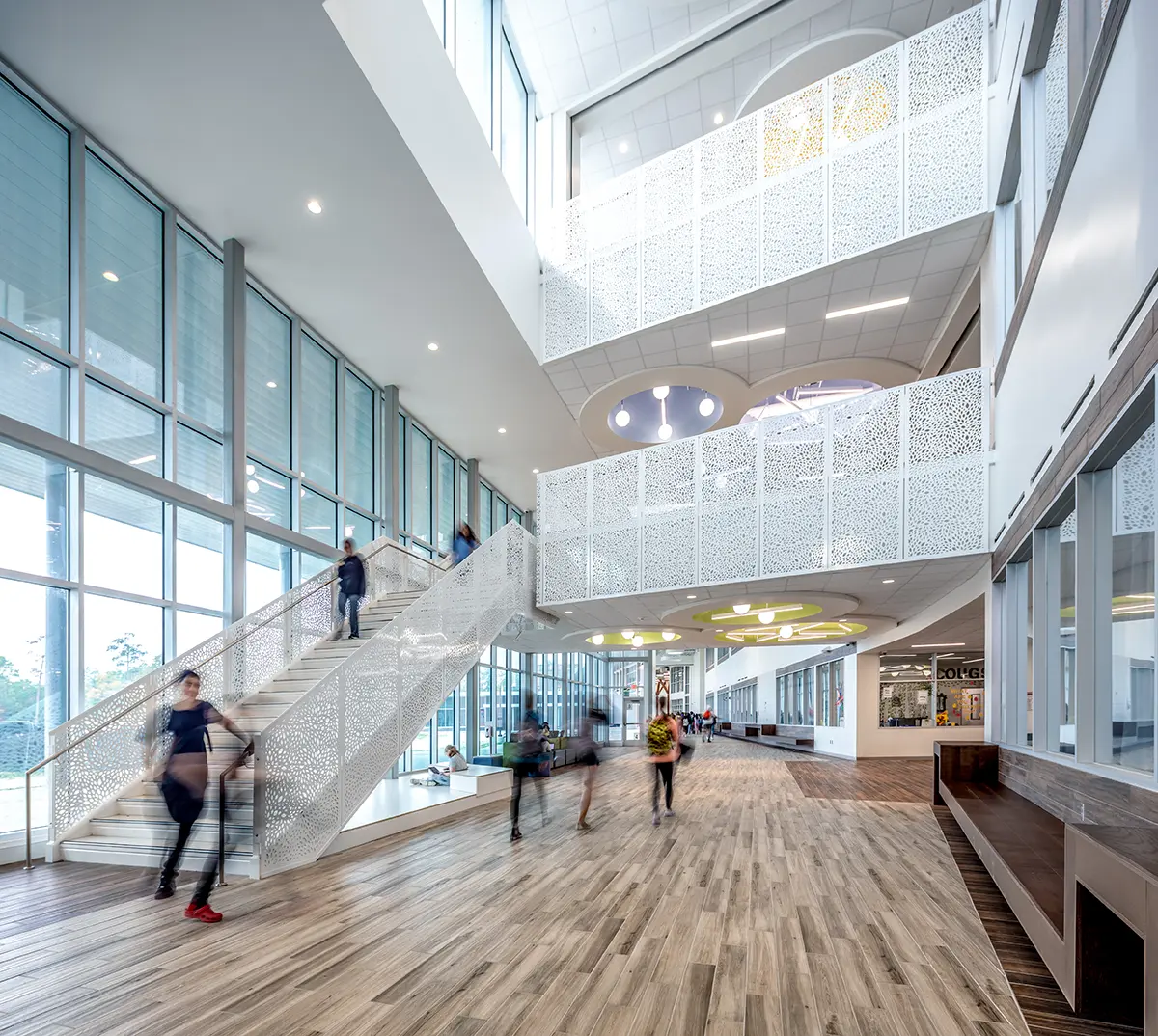 Modern building interior with high ceilings and large windows. People move on a staircase with intricate railing designs. Bright and spacious ambiance.