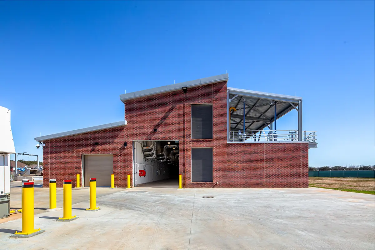 A modern red brick industrial building with an open garage, yellow bollards in front, and a clear blue sky, conveying functionality and simplicity.