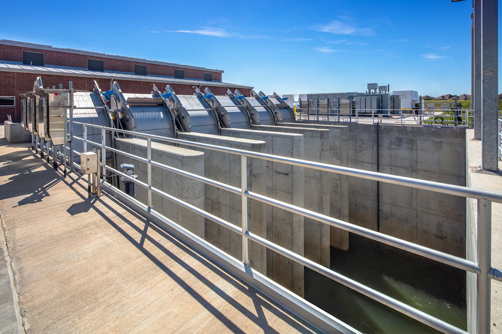 Industrial water treatment facility under clear blue skies, showcasing large metal machinery and concrete tanks. The scene conveys efficiency and modern infrastructure.