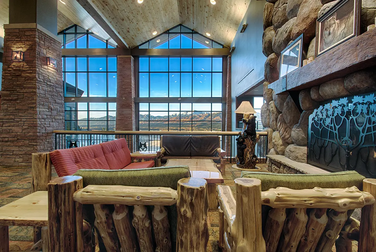 Rustic lodge interior with wooden furniture, stone fireplace, and large windows showcasing a mountain view. Cozy and inviting atmosphere.