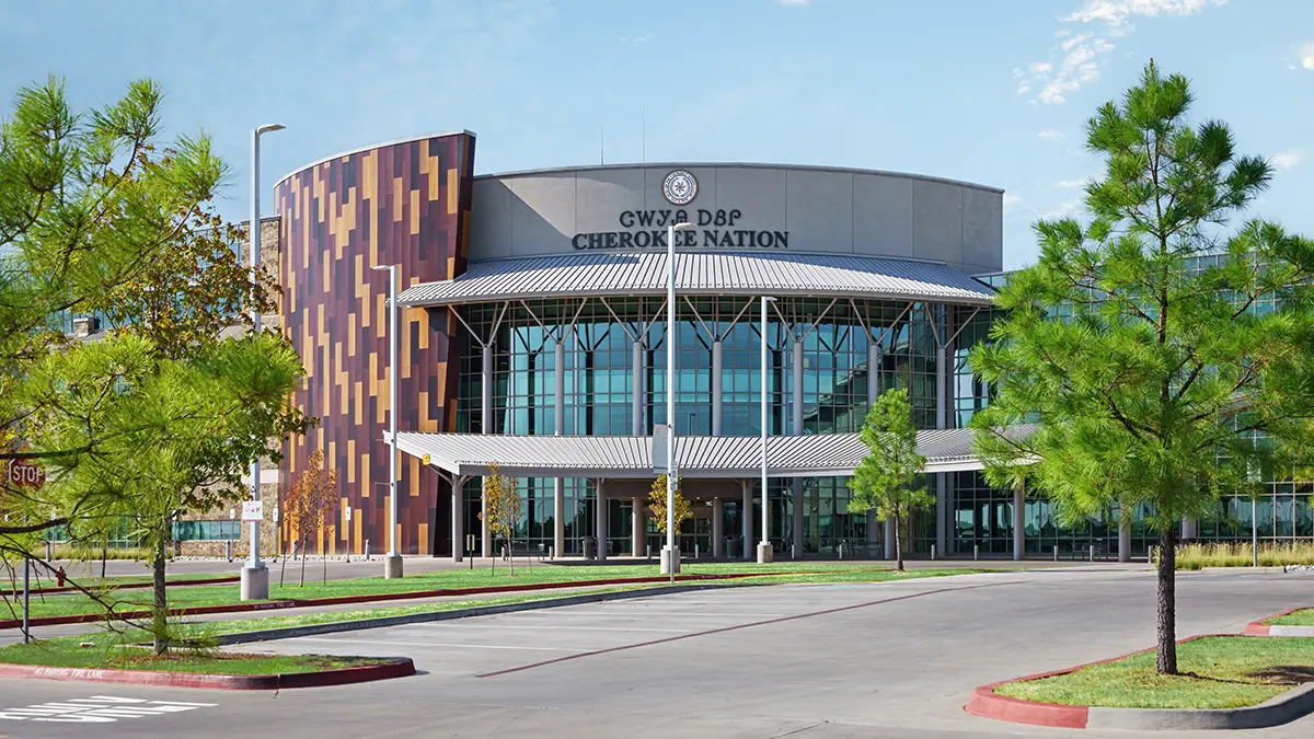 Modern building with a curved, colorful facade and tall glass windows, surrounded by green trees. The sign says "Cherokee Nation," evoking pride and community.