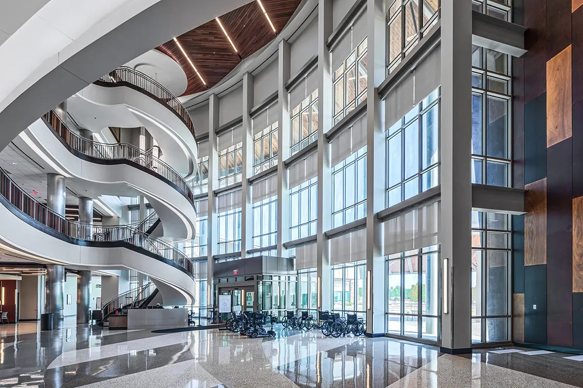 Spacious modern atrium with high ceilings, large windows, and a sweeping spiral staircase. Sunlight streams in, reflecting on polished floors. Tranquil atmosphere.