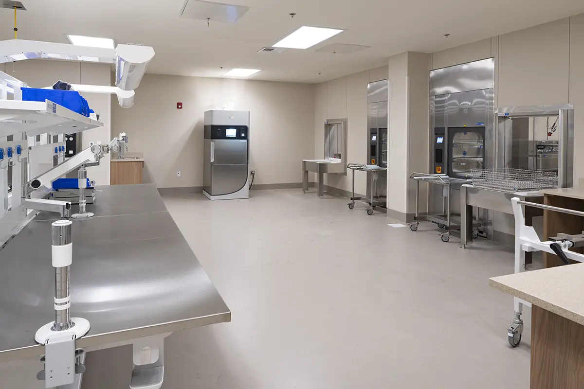 Spacious, sterile laboratory with stainless steel tables, advanced equipment, clean floors, and bright overhead lighting, conveying a clinical, modern tone.