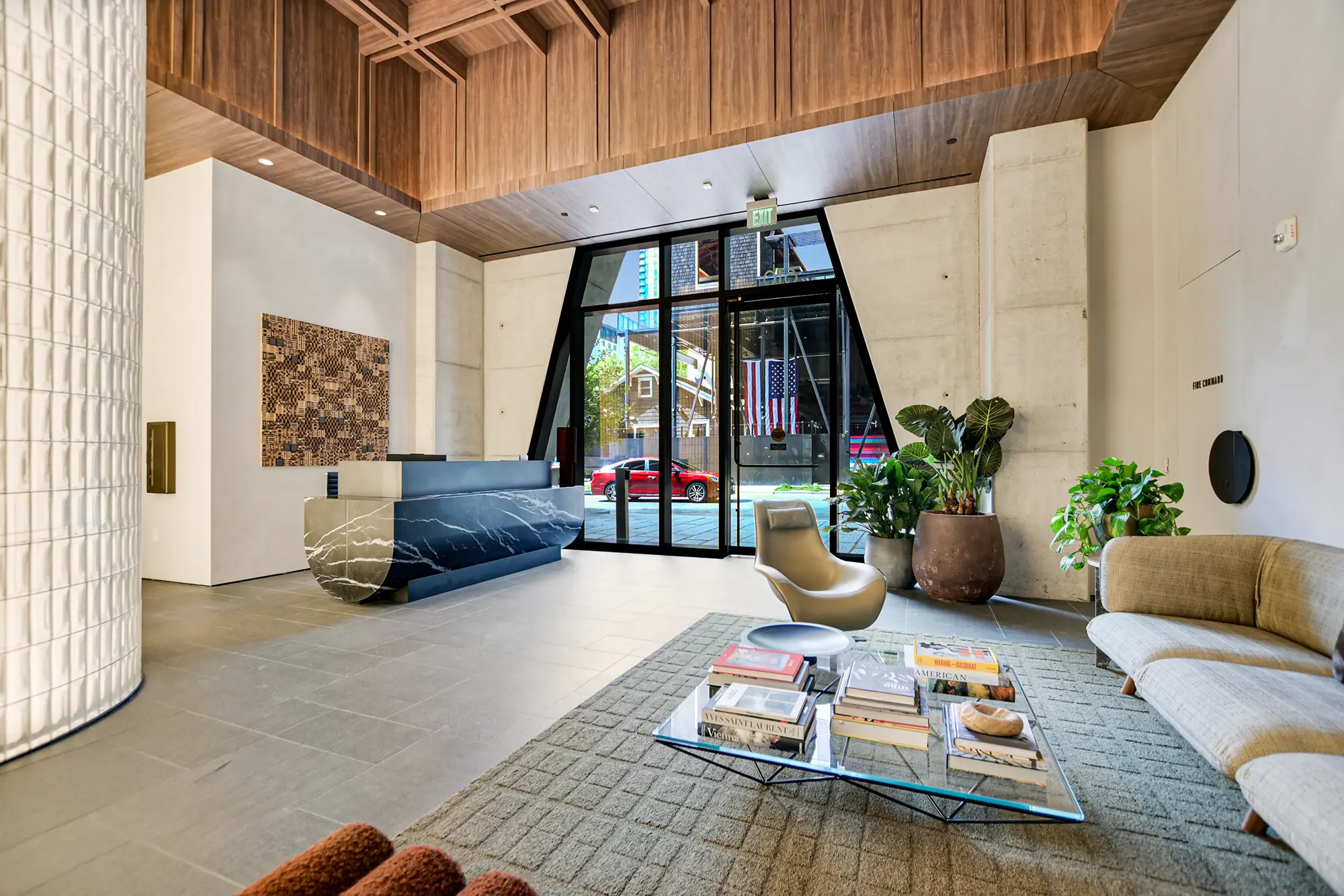 Modern lobby with large glass doors, a sleek marble reception desk, stylish furniture, and lush plants. Bright, welcoming ambiance with a city view.