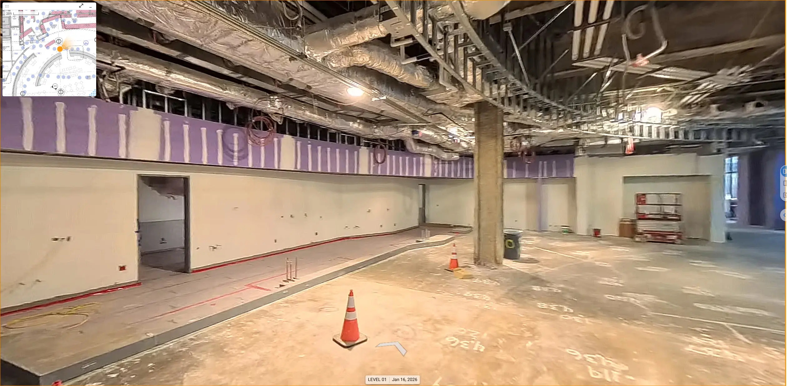 Construction site with exposed ductwork and wiring on the ceiling. Unfinished walls and floors, with traffic cones and scribe marks, suggest ongoing work.