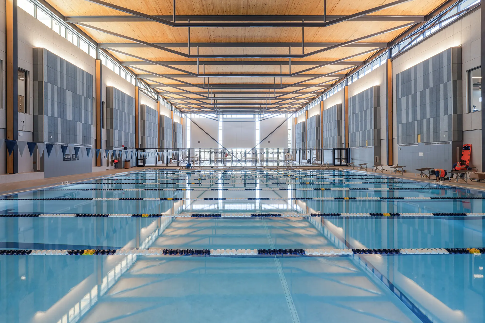 Spacious indoor swimming pool with multiple lanes, surrounded by modern architecture featuring wooden ceilings and large windows, creating a calm atmosphere.