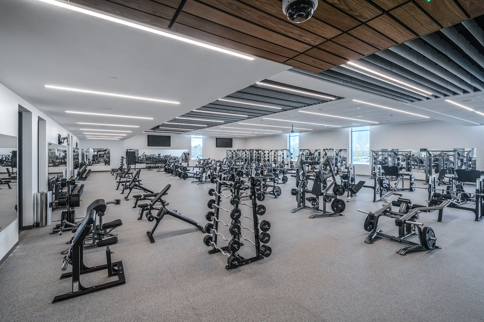 Spacious gym with rows of weightlifting equipment, benches, and mirrors. Bright lighting and modern design create an inviting, energetic atmosphere.