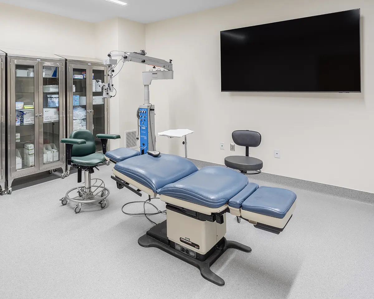 Surgical room with a blue operating table, overhead light, and equipment cabinets. Clean, sterile environment; calm, professional atmosphere.