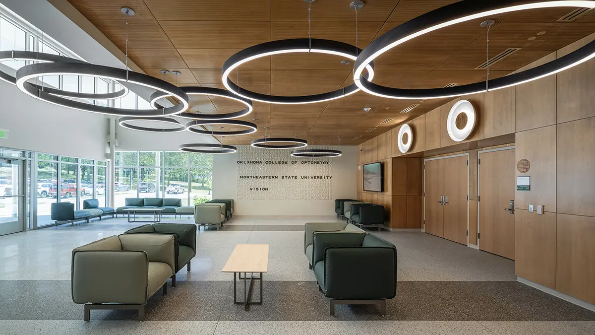 Modern lobby with green couches, wooden ceiling, and circular pendant lights. Bright and spacious, with large windows and a welcoming atmosphere.