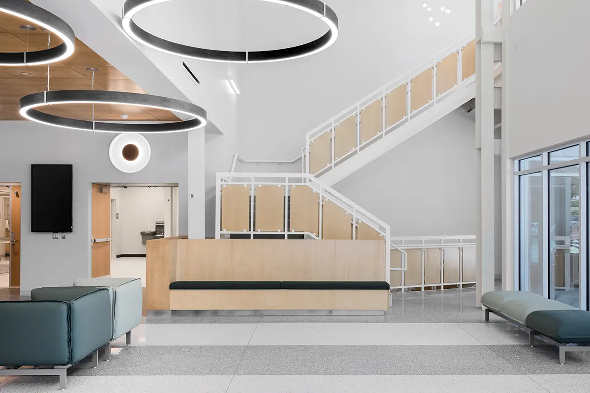Modern lobby with minimalist design, featuring large circular ceiling lights, gray seating, a wooden staircase, and a sleek, open atmosphere.